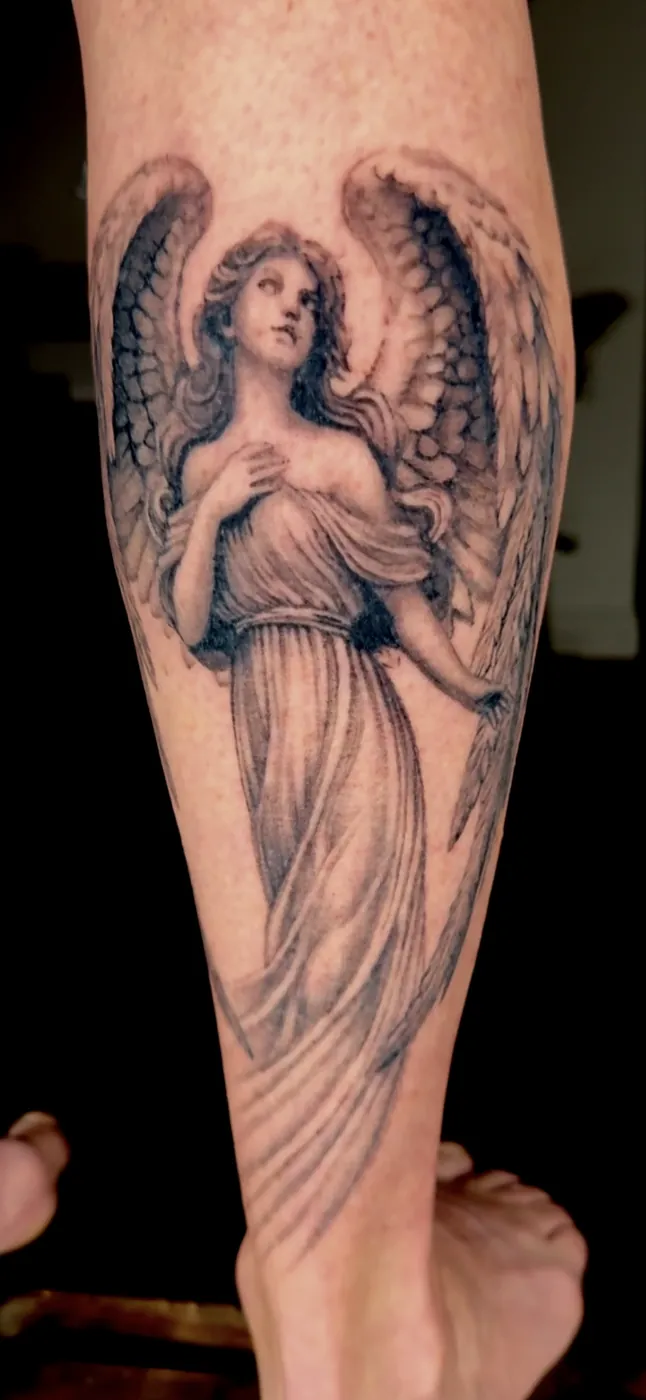 Ange statuaire tatoué sur le mollet, style gravure noir et gris.