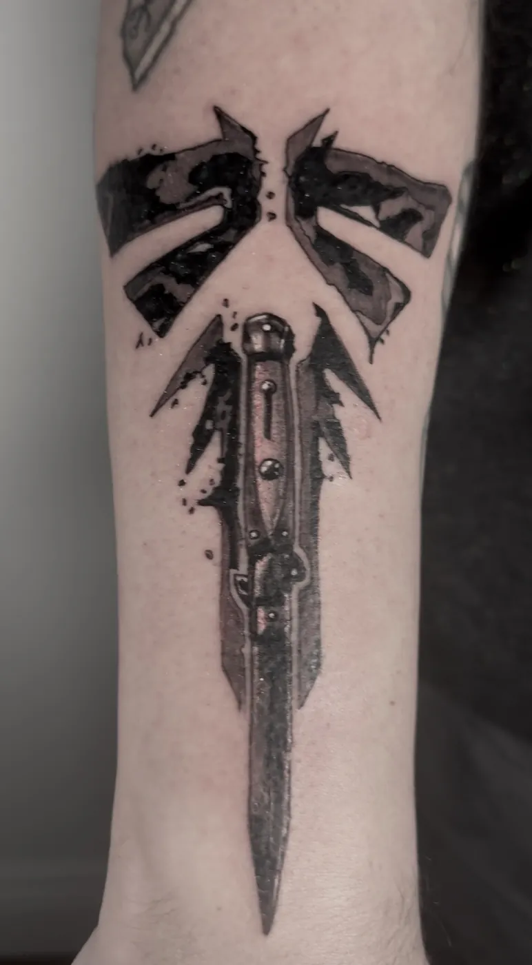 Insigne déchiré et couteau à cran d'arrêt, tatoués sur l'avant-bras, linework noir et gris.