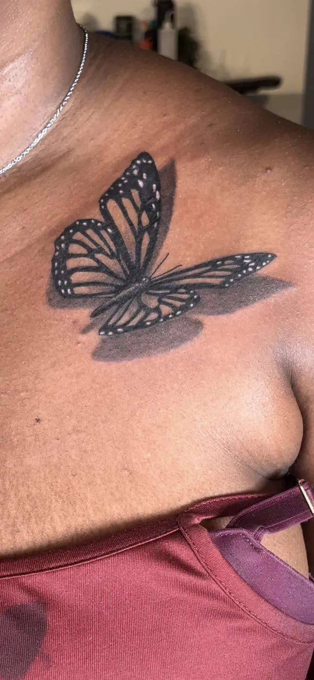 Papillon monarque en relief avec ombre portée, tatoué sur la clavicule.